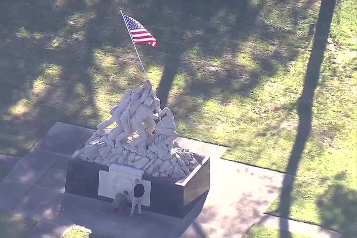 Aerial view of the Iwo Jima statue in Quantico, Virginia, with an American flag above the stone Marines and two people examining the monument’s base